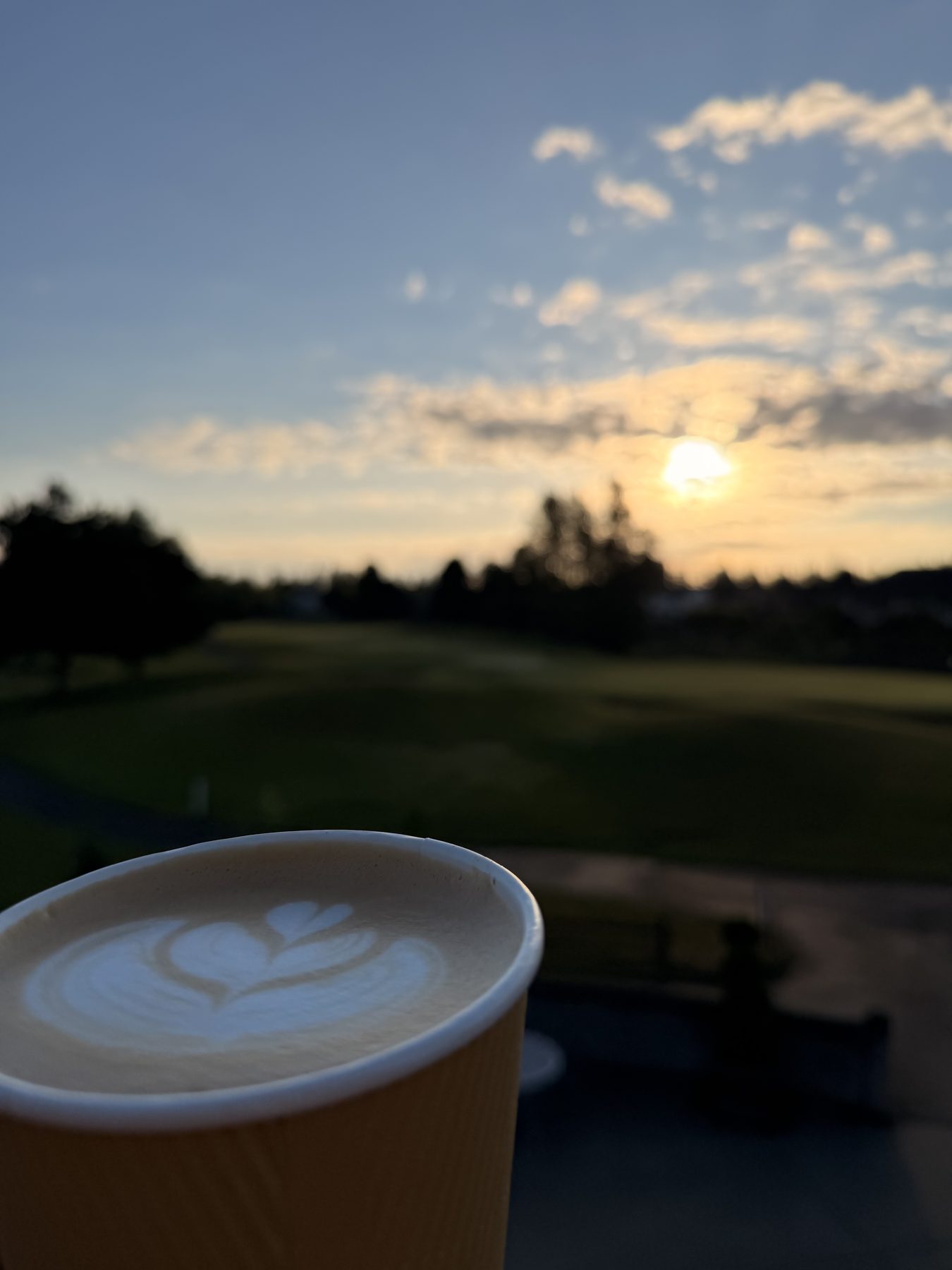 A latte on the rail at sunrise, the course behind it